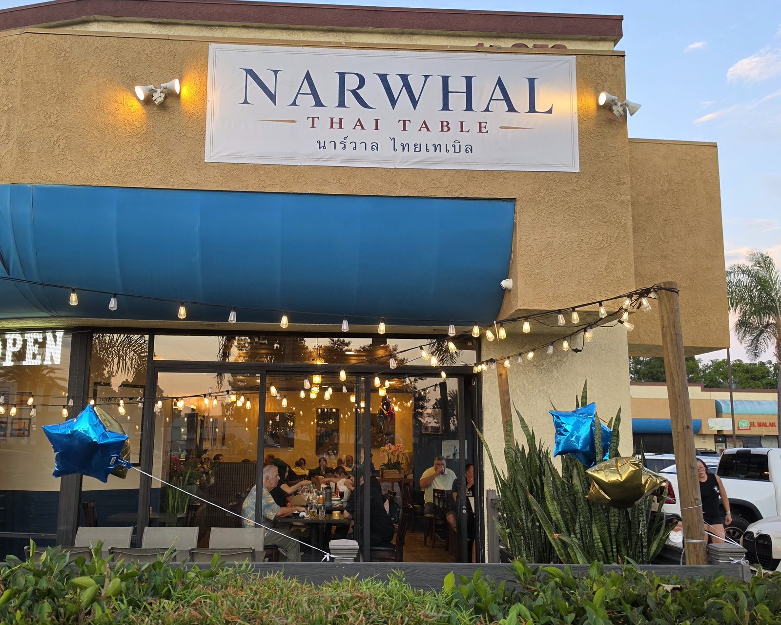 Narwhal Thai Table storefront on Beach Blvd, Huntington Beach, at dusk with string lights over the patio